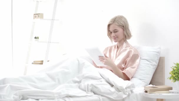 有吸引力的金发年轻女子使用数字平板电脑和微笑 而坐在床上 — 图库视频影像
