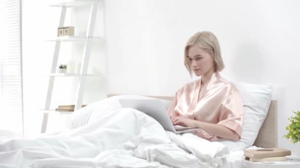 有吸引力的金发女孩使用笔记本电脑 微笑和触摸的脸 而坐在床上 — 图库视频影像