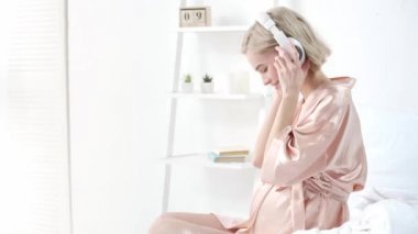 neşeli sarışın hamile kadın müzik dinleme, kulaklık çıkarma ve karın yakınında tutarak 