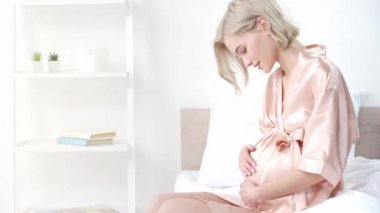 neşeli sarışın hamile kadın karın dokunmadan ve yatak odasında otururken gülümseyen