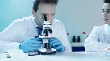 yakışıklı bilim adamı mikroskop ile analiz yapma ve laboratuvarda yakın oturan güzel doktor konuşuyor