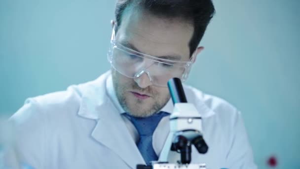 Cientista Bonito Óculos Proteção Fazendo Análise Com Microscópio Anotando Resultados — Vídeo de Stock
