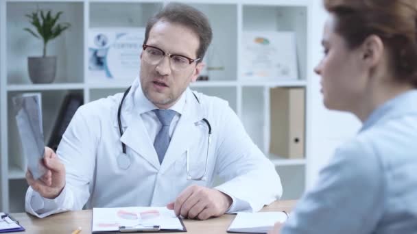職場に座っている深刻な医師の選択的な焦点 X線診断を見て アシスタントに話す — ストック動画