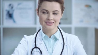 beyaz ceketli neşeli genç doktor gülümseyerek ve kameraya bakarak 