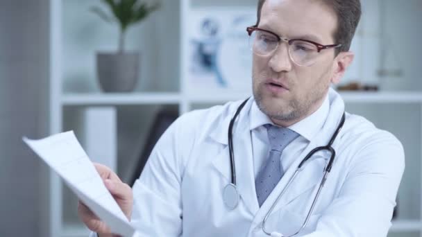 Médico Serio Con Estetoscopio Hablando Mientras Mira Papel Con Cardiograma — Vídeo de stock