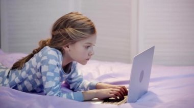 dizüstü bilgisayar klavyesi üzerinde yazarken yatakta yatan pijama preteen çocuk, el ile yüz propping, gülümseyerek ve ekranda parmak ile işaret
