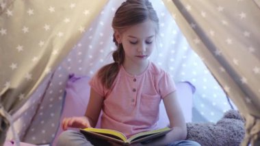 sevimli odaklı preteen çocuk wigwam oturan ve kitap okuma