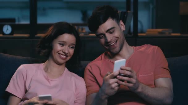 开朗的年轻男人和女人使用智能手机 说话和微笑 而坐在家里的平板电脑 — 图库视频影像