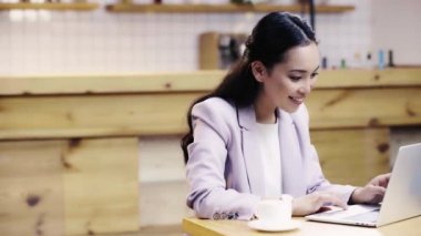 kafede dizüstü bilgisayar kullanarak takım elbise içinde gülümseyen ve güzel Asyalı iş kadını 