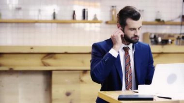 takım elbiseli yakışıklı ve gülümseyen adam müzik dinleyerek ve kafede dizüstü bilgisayar kullanarak 