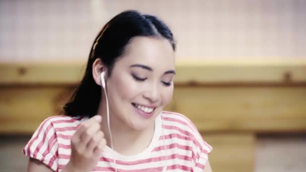 カフェで音楽を聴いているTシャツで笑顔とかわいいアジアの女性 — ストック動画