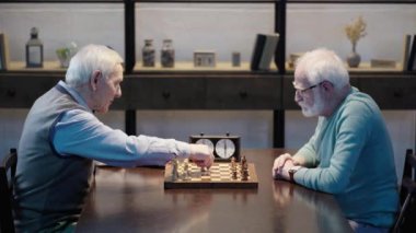 masada oturan, satranç oynayan ve oturma odasında satranç saatine basan iki dalgın üst düzey adamın yan görünümü