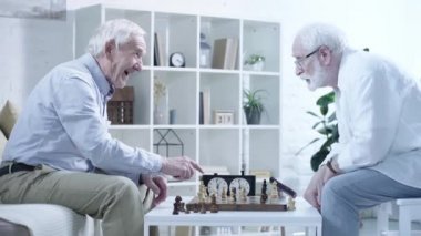 oturma odasında dalgın arkadaşı ile satranç oynarken gülen yaşlı adamın yan görünümü