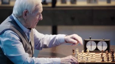 yelekli yaşlı adamın arkadaşıyla satranç oynaması, satranç saatine basıp oturma odasında gülme
