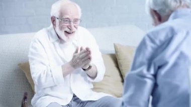 gözlük heyecanlı kıdemli adam ellerini ovuşturarak, arkadaş bakarak ve oturma odasında el sıkışma