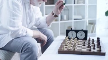 satranç oynarken ve satranç saati üzerinde düğmeye basarak kol saati kıdemli adam kırpılmış görünümü