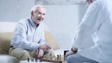 oturma odasında arkadaşı ile satranç oynarken gülen mavi gömlekli kıdemli adam