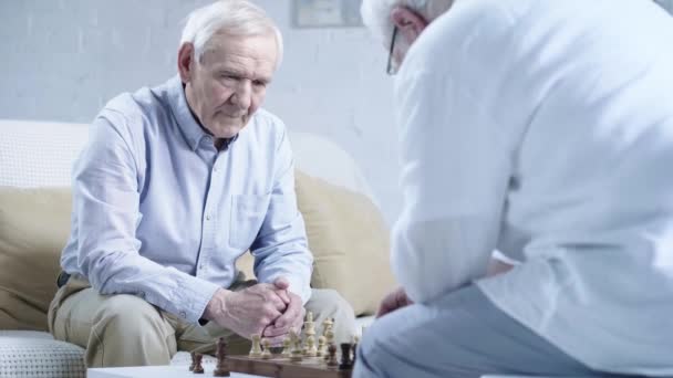 Två Seniora Män Skjortor Pratar Medan Spelar Schack Vardagsrummet — Stockvideo