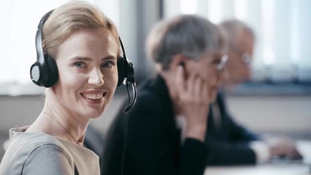 Kulaklıkneşeli Teleworker Kamera Bakarak Ofiste Arkadaşları Yakınında Gülümseyerek — Stok video