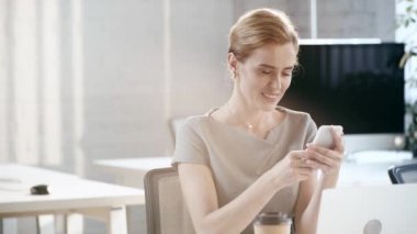 çekici kadın gülümseyen ve ofiste akıllı telefon kullanarak 