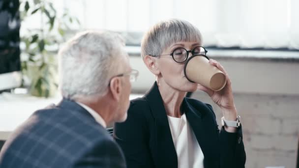 紙コップを持ったメガネの女性の選択的な焦点 行くためにコーヒーを飲む 男性を見て オフィスで笑顔 — ストック動画