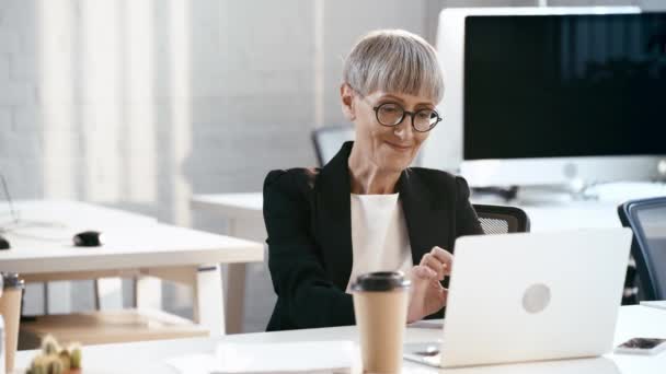 Atrakcyjna Kobieta Okularach Uśmiechnięta Pobliżu Laptopa Kubek Papieru Biurze — Wideo stockowe