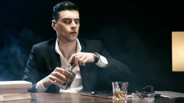 真面目なビジネスマンのオープニングボトル ガラスにウイスキーを注ぎ 黒のテーブルでペンを飲んで保持 — ストック動画