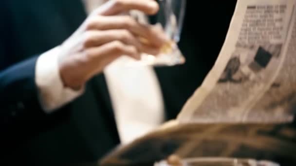 ビジネスマンが新聞を読み 黒で隔離されたテーブルでウイスキーを飲む — ストック動画