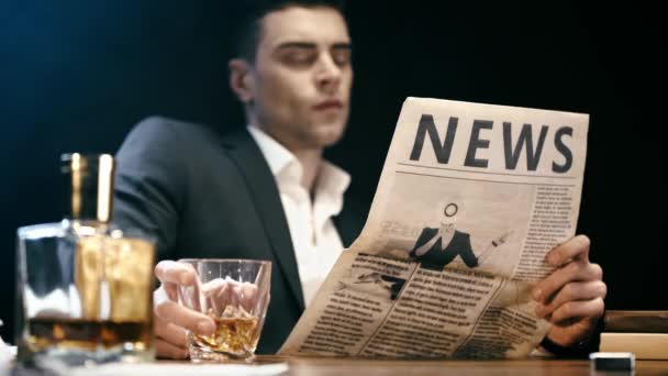selective focus of businessman reading newspaper and drinking whiskey at table on black