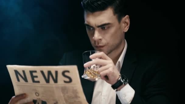 集中的商人坐在桌子上的烟灰缸 看报纸和喝威士忌在黑烟 — 图库视频影像