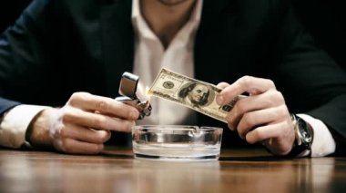 ahşap masada kül tepsisi yukarıda hafif ve yanan dolar banknot tutan işadamı kırpılmış görünümü