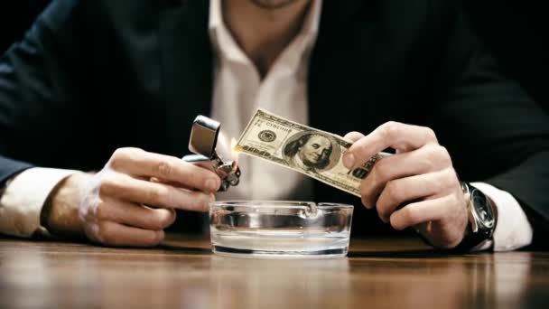 木製のテーブルの灰皿の上にライターと燃えるドル紙幣を保持しているビジネスマンのトリミングされたビュー — ストック動画