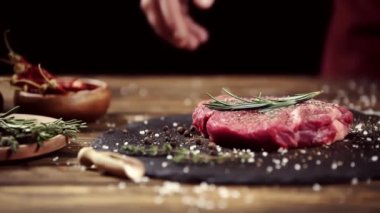 Siyah üzerinde izole baharat ve biberiye ile süslenmiş çiğ et biftek ile plaka alarak adam kırpılmış görünümü