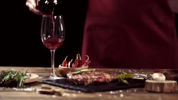 geschnittene Ansicht eines Mannes, der Wein in Glas gießt, in der Nähe von Fleischsteak und Zutaten auf einem Tisch isoliert auf schwarz