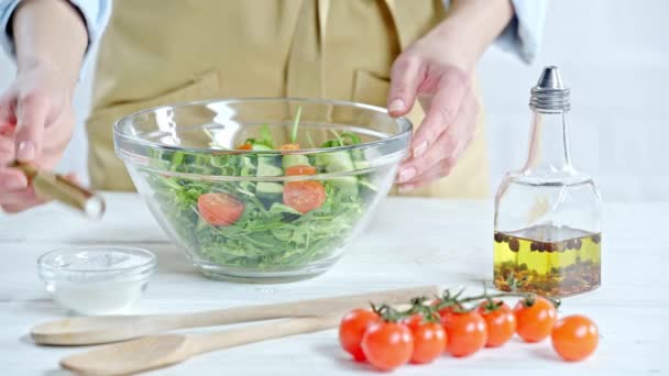 裁剪视图的妇女调味蔬菜沙拉与盐附近的成分在桌子上 — 图库视频影像