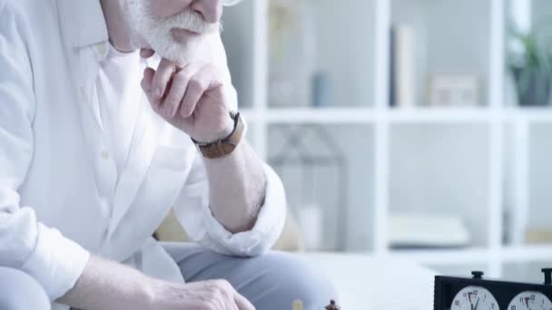 zkušený starší muž, který klepat na stůl a pozoroval protivníka, jak se při hraní šachy v obývacím pokoji pohne