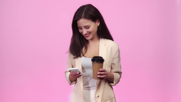 Menina Bonita Usando Smartphone Sorrindo Bebendo Café Para Isolado Rosa — Vídeo de Stock