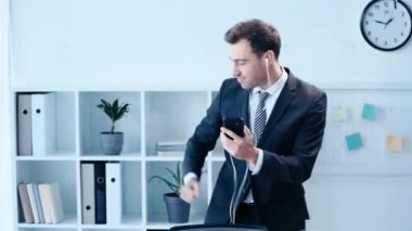 kulaklıklar ve akıllı telefon ile müzik dinlerken ofiste neşeli işadamı dans