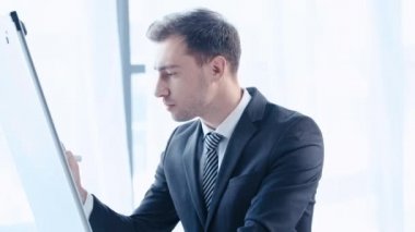 Ofis flipchart üzerinde keçe kalem ile yakışıklı, konsantre işadamı yazma