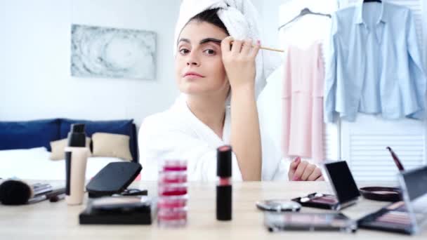 装飾的な化粧品でテーブルの近くに眉毛をブラッシングする女性 — ストック動画