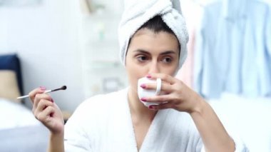 bornozlu kadın göz farı uygulayarak ve kahve içerek