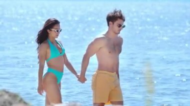 deniz kenarında yürürken el ele tutuşan ve gülümseyen mutlu genç çift 