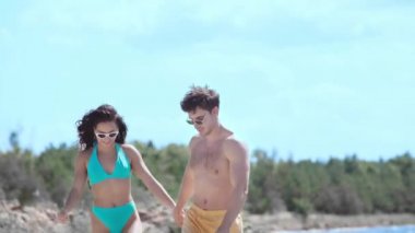 deniz kenarında yürürken el ele tutuşan ve konuşan mutlu genç çift