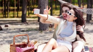 neşeli genç çift akıllı telefonda selfie çekmek ve plajda dinlenirken zafer jestleri gösteren