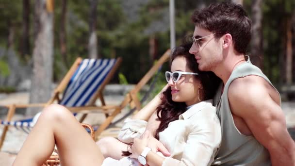 英俊的年轻人拥抱女朋友 并指着手指 而休息在海滩上 — 图库视频影像
