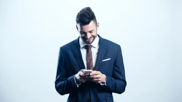 ハンサムなビジネスマンは笑顔と白にスマートフォンを使用しています — ストック動画