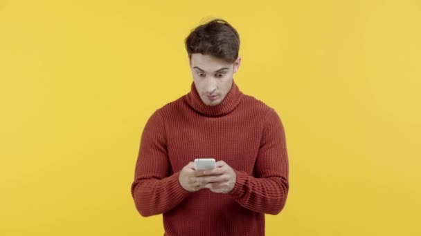 黄色で隔離されたスマートフォンでセーターのテキストメッセージでショックを受けた男 — ストック動画