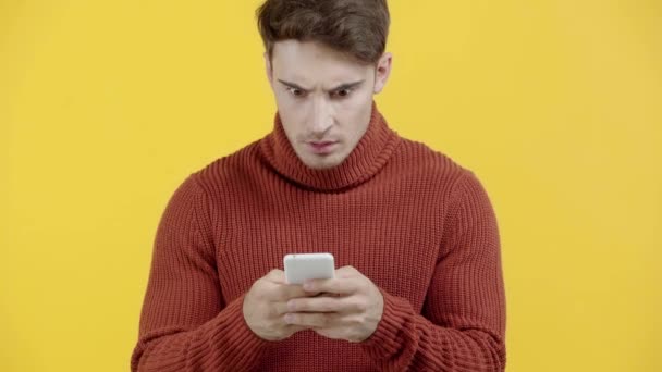 黄色で隔離されたスマートフォンでセーターのテキストメッセージで驚いた男 — ストック動画