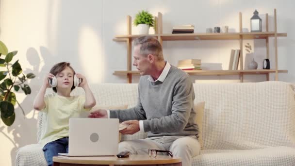 grandfather offering grandson to read book while boy listening music in headphones