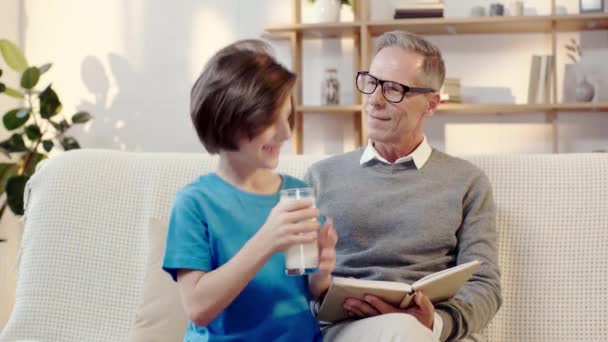 Abuelo Leyendo Libro Abrazando Con Nieto Que Bebe Leche — Vídeo de stock